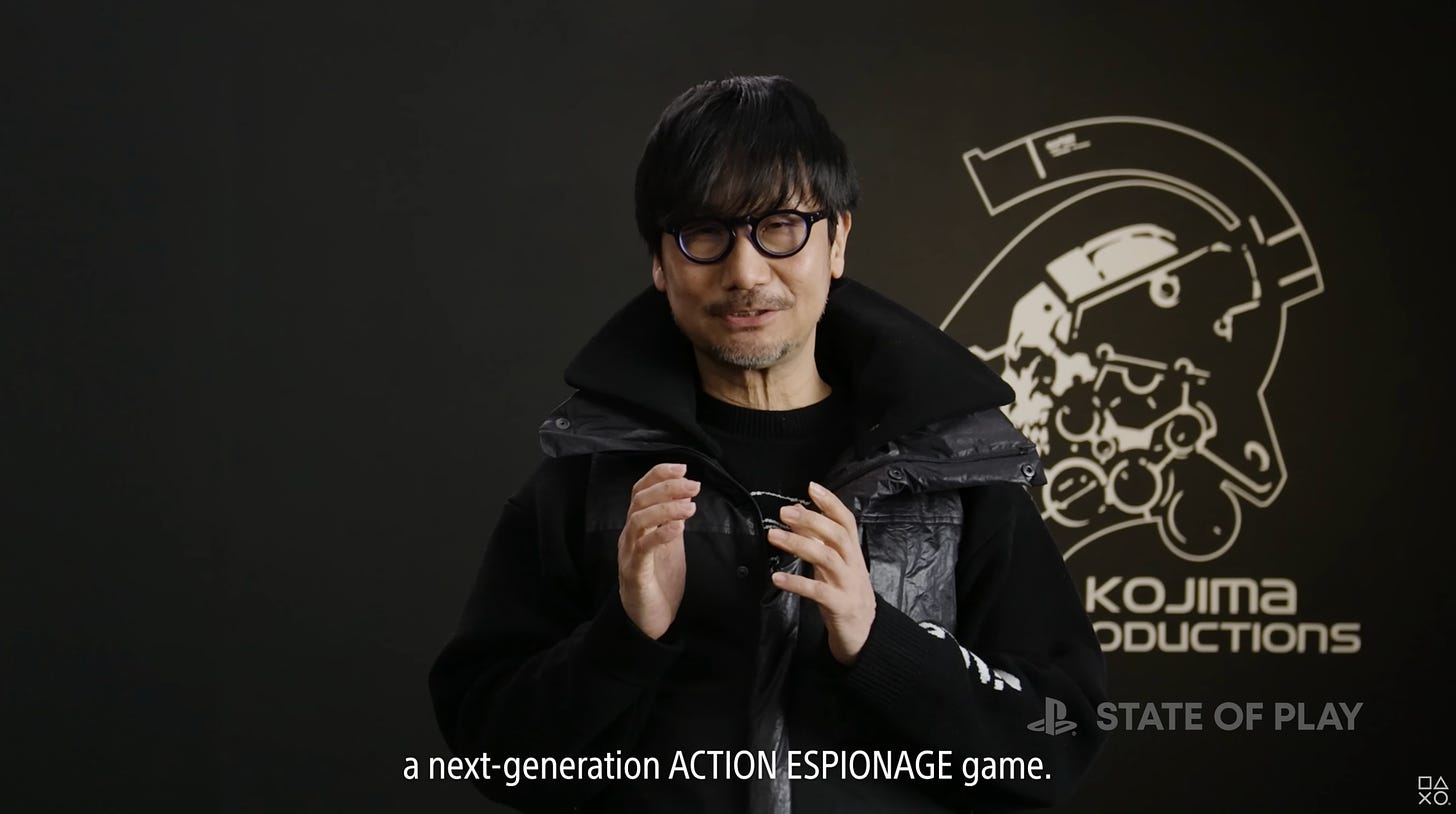 Video screenshot of Hideo Kojima in a heavy coat, gesturing with this hands. The subtitles "a next-generation ACTION ESPIONAGE game." appear below him.