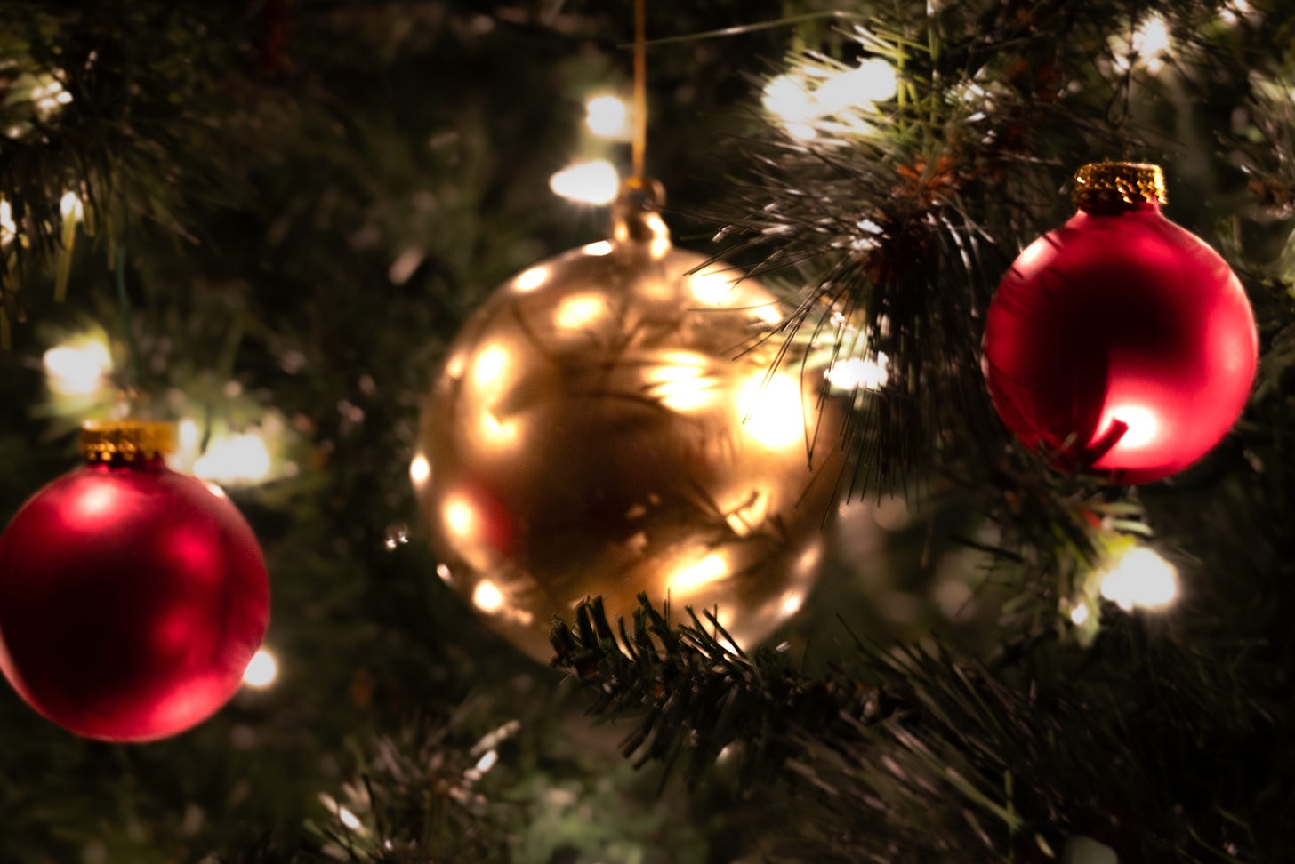 One gold and two red ornaments sparkle against the lights on a Christmas tree