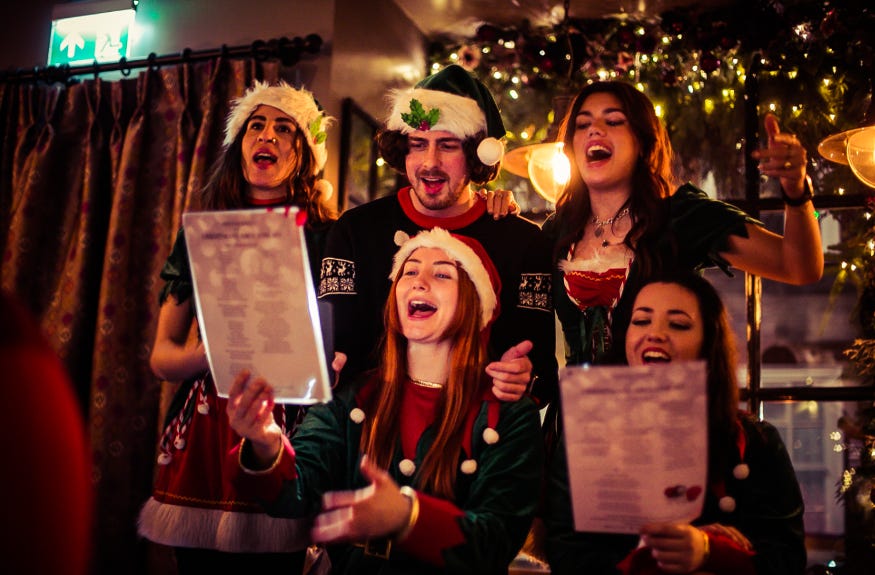 Five carollers singing in front of a Christmas tree