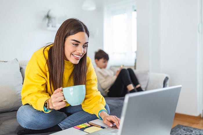 A woman holding a coffee and working on a laptop.