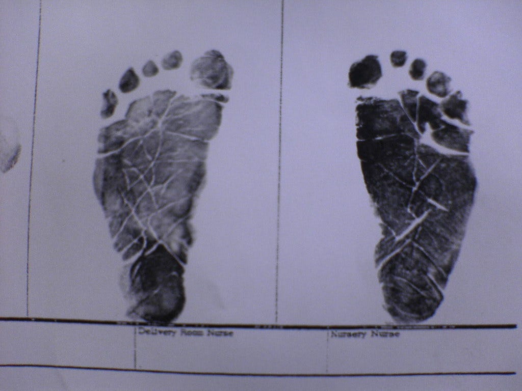 Black prints of a newborn's feet from a hospital form. "feet" by Eric is licensed under CC BY-NC-SA 2.0.