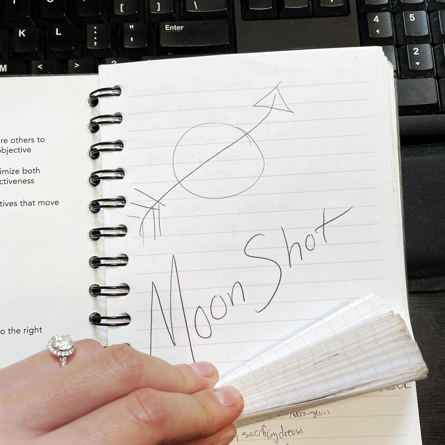 a journal on a black desk opened to a page with Moonshot written across it in large lettering