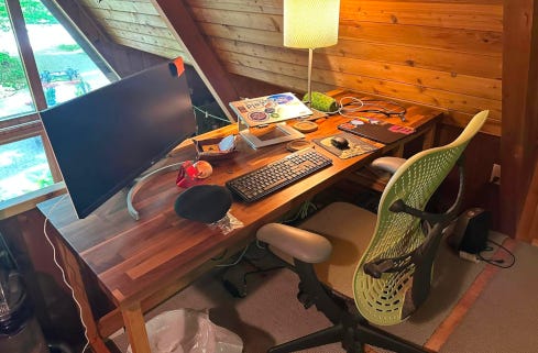 A desk with a chair, monitor, and laptops