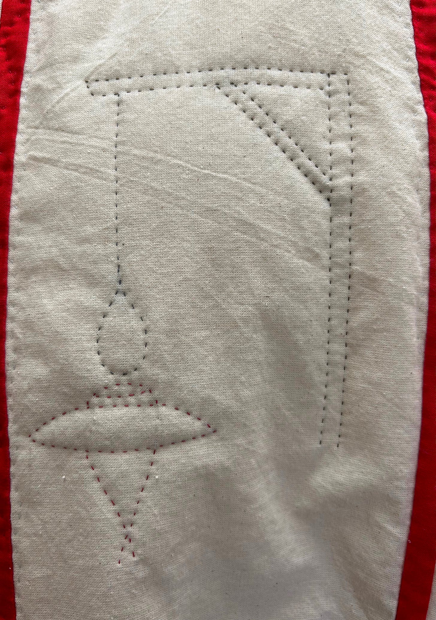 Gallows, a noose, and a cardinal’s hat, handstitched on to cream fabric.