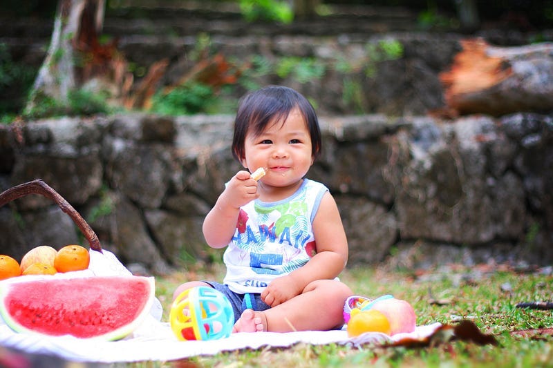Child sitting on blanket and eating food.
