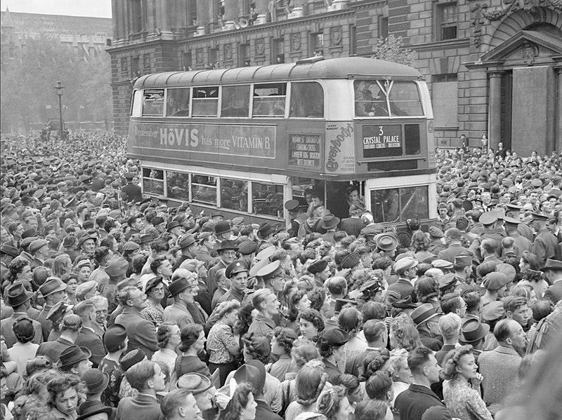 A number 3 double-decker bus slowly pushes its way through the huge crowds gathered in Whitehall to hear Churchill's Victory speech and celebrate Victory in Europe Day