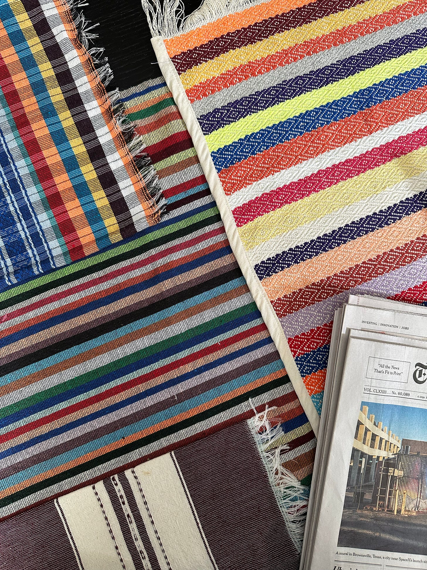 Tight shot of a table with four different colorful placemats and part of a newspaper