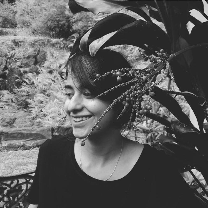 A photo of Rohini smiling away from the camera with foliage covering a part of their face.