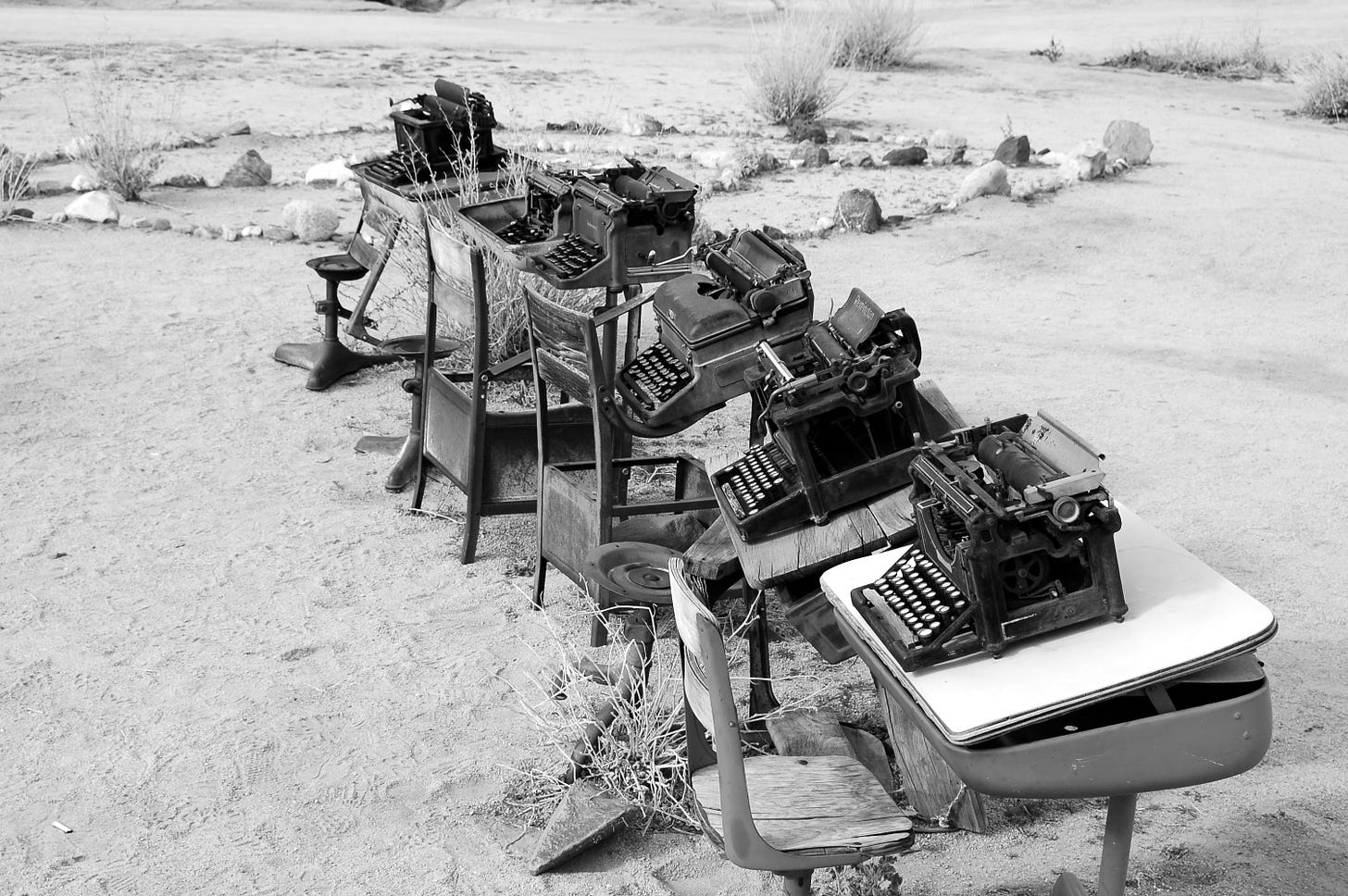 black and white photo of vintage black typewriters on vintage desks in dessert