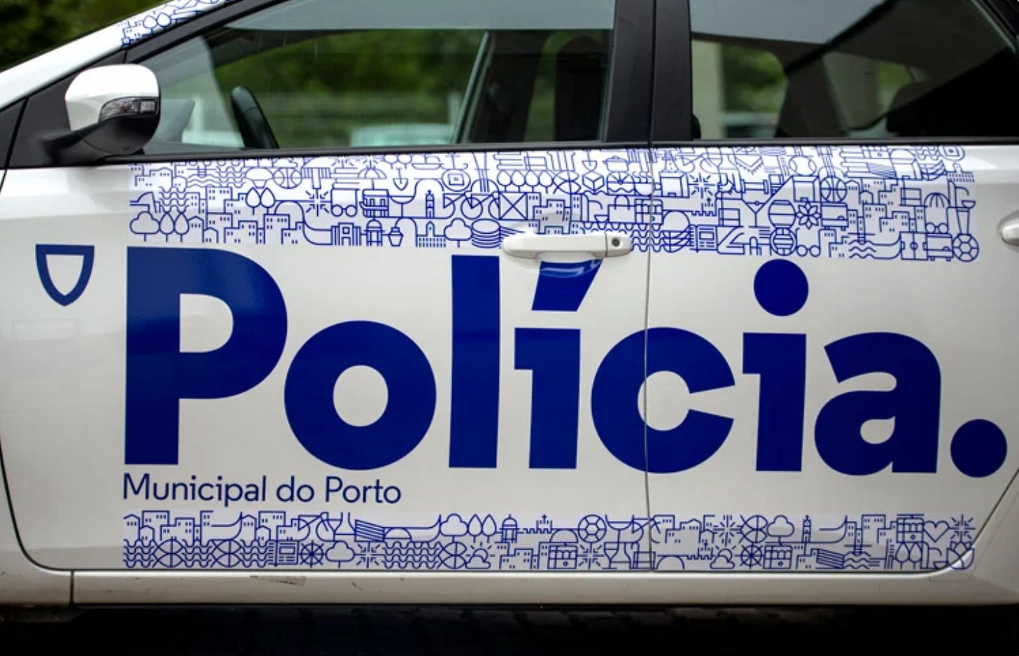 La portiera di un'auto della polizia municipale di Porto: il logo è dello stesso azzurro e dice Polícia. sempre con il punto finale.