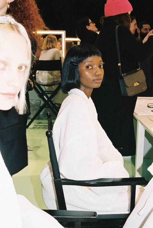 This may contain: two women sitting at a table in front of other people, one with black hair and the other wearing white