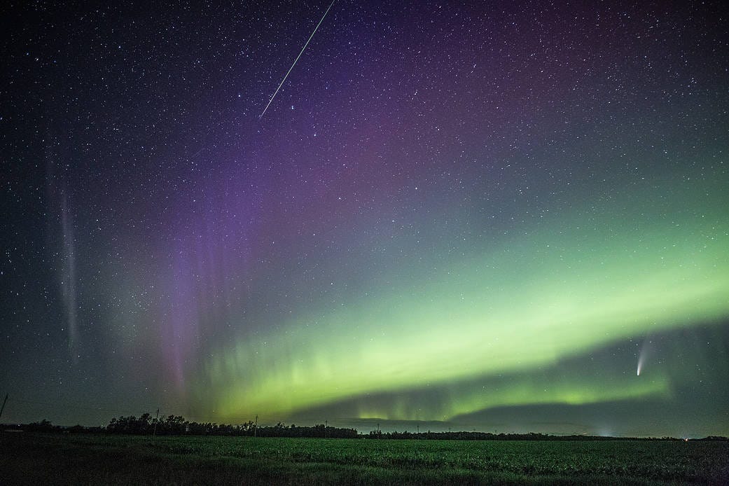 Comet NEOWISE appears in a sky streaked with purple and green aurora