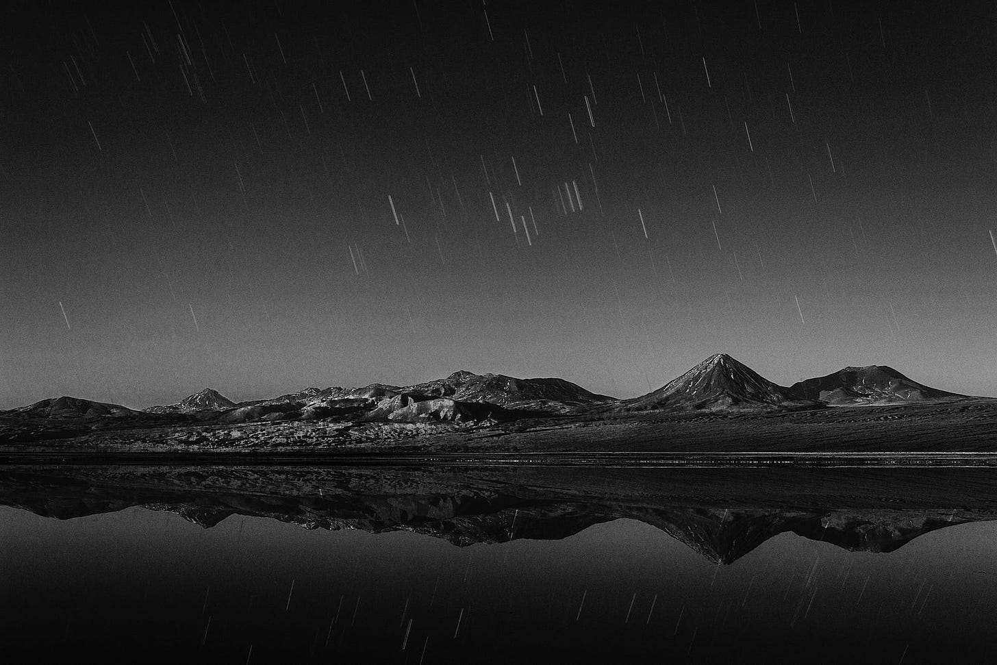 A meteor shower photographed over a lake reflecting mountains.