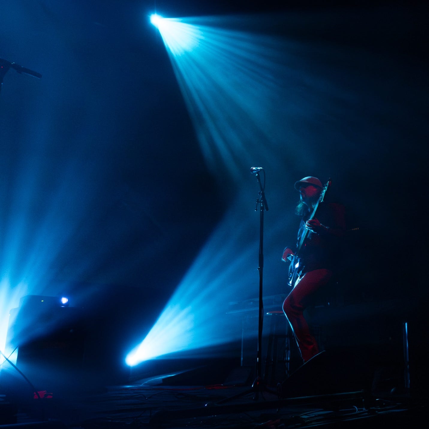 A person playing guitar on stage with blue lights

Description automatically generated