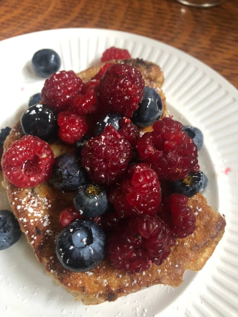 A white plate with french toast topped with raspberries and blueberries