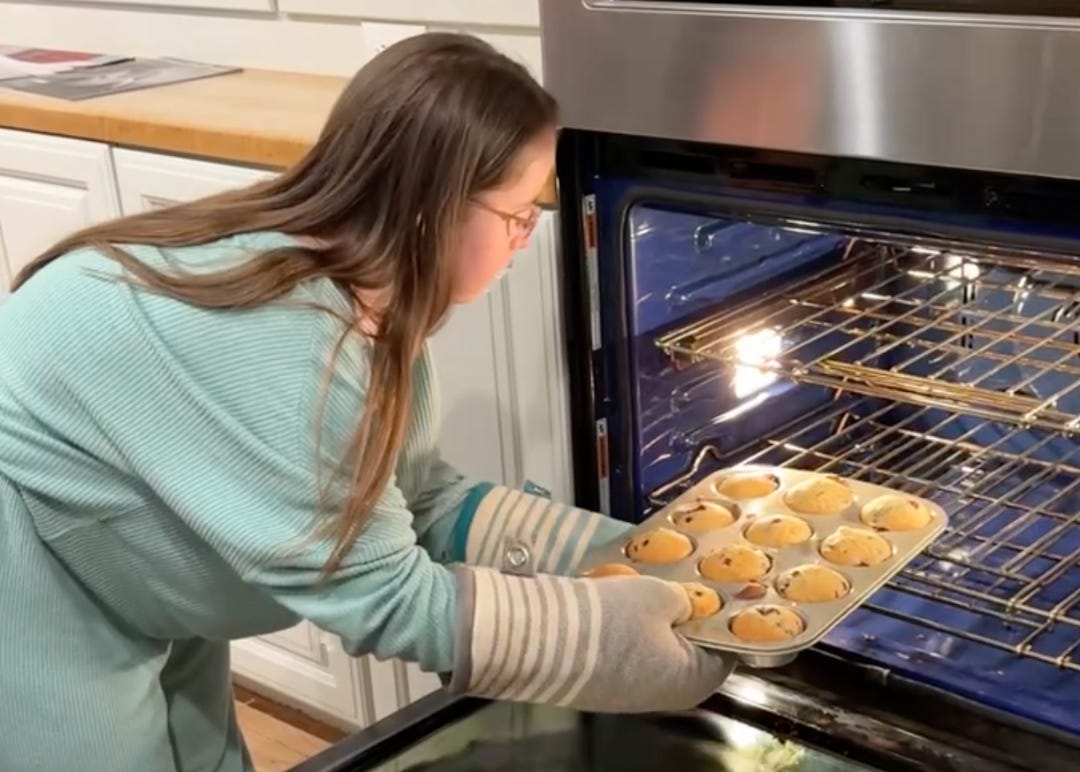 Penny taking muffins out of the oven