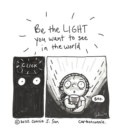 Be the Light Short black and white comic strip with the hand-drawn accented heading "Be the LIGHT you want to see in the world," followed by a panel painted in entirely in inky black, except for two bulging white cartoon eyes and the sound of a "click." The last panel shows a stage-lit cartoon girl with a braid, holding a flashlight under her face, looking spooky. A single speech bubble says, "Boo." Webcomic by Connie Sun, cartoonconnie, 2022.