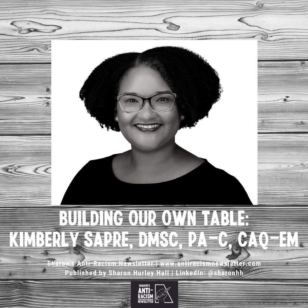 Building Our Own Table: Kimberly Sapre, DMSc, PA-C, CAQ-EM - Black and white photo of Kimberly Sapre with natural curly hair and glasses. She is smiling and wearing a dark top