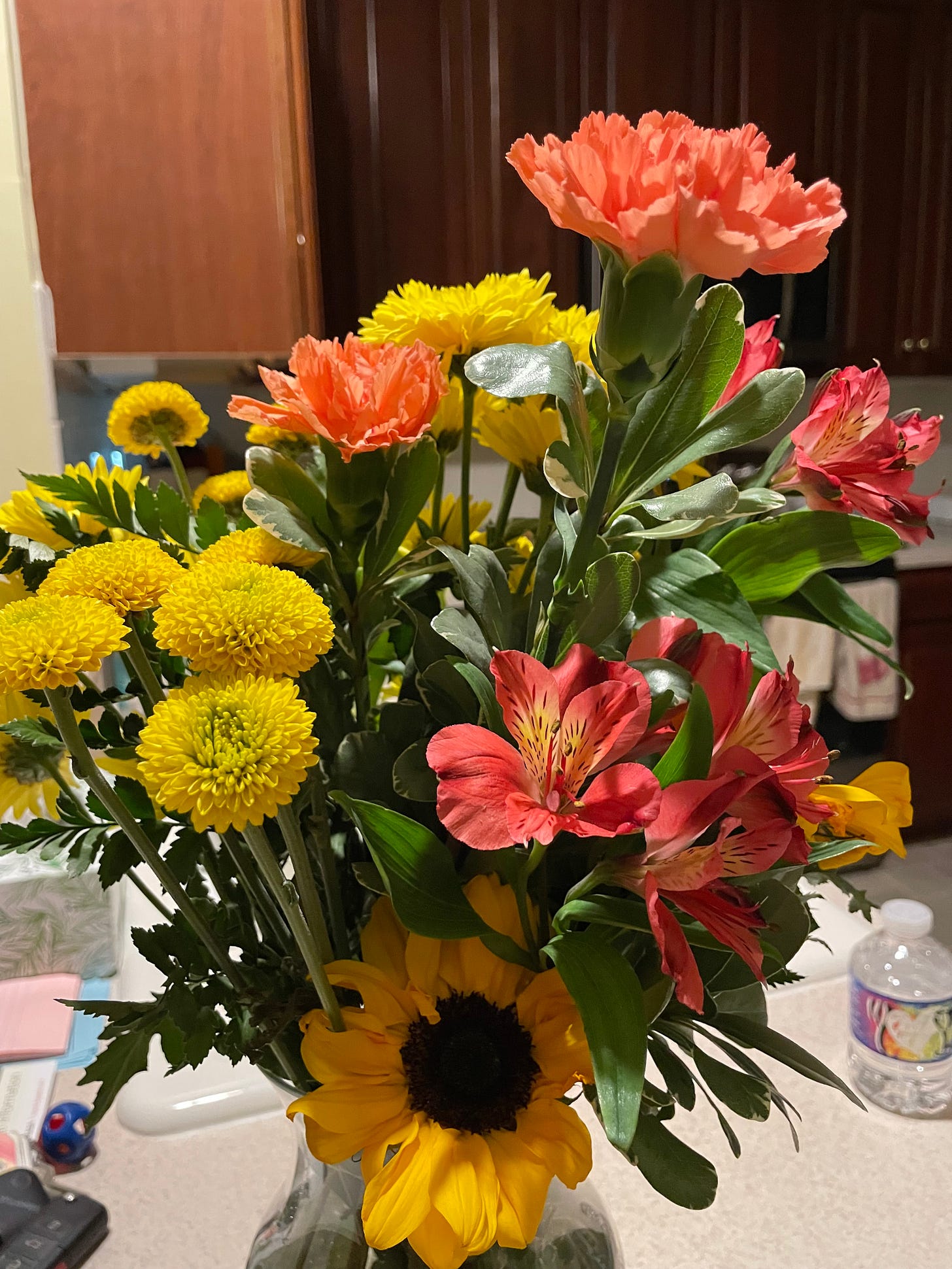A bouquet of yellow and orange-red flowers in a vase, placed on a kitchen counter.