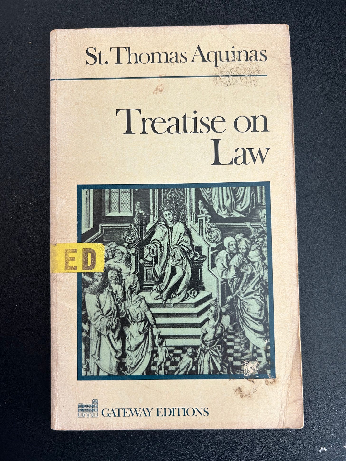 A battered copy of the Treatise on Law by St. Thomas Aquinas, with a yellow "Used" sticker visible on the front cover.