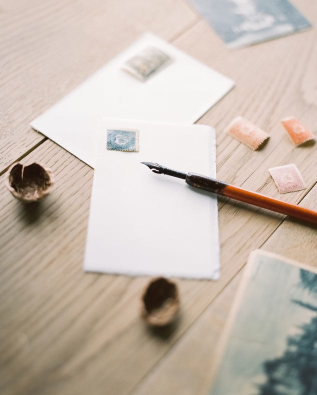 envelopes with stamps on them on a wooden table, a fountain pen alongside them