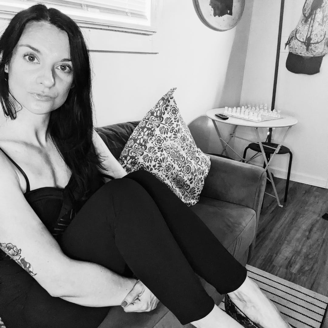 A woman sitting on a couch with a chess set in the background.