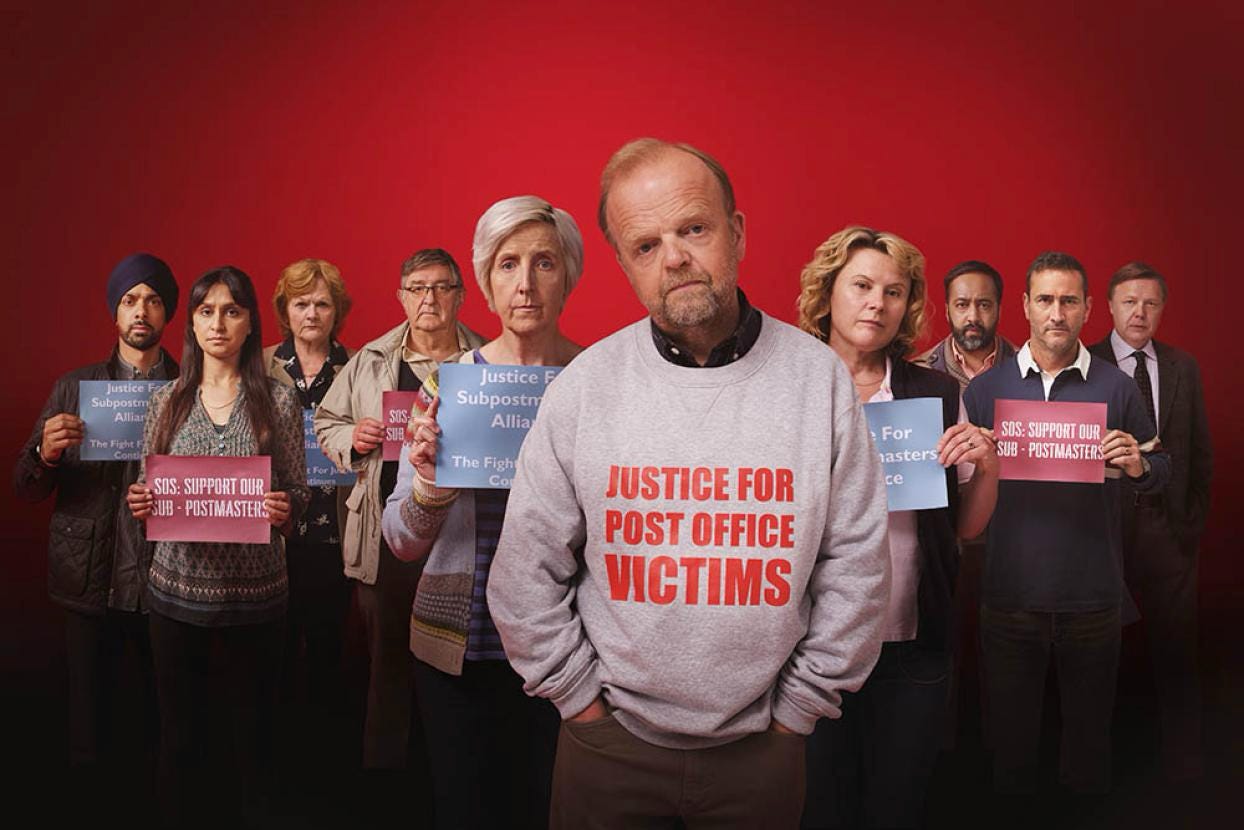 A promo picture for Mr. Bates vs the Post Office. It features a phalanx of concerned-looking adults holding papers with slogans supporting the subpostmasters. Mr. Bates stands in the foreground in a gray sweater with "JUSTICE FOR POST OFFICE VICTIMS" written in red all caps.