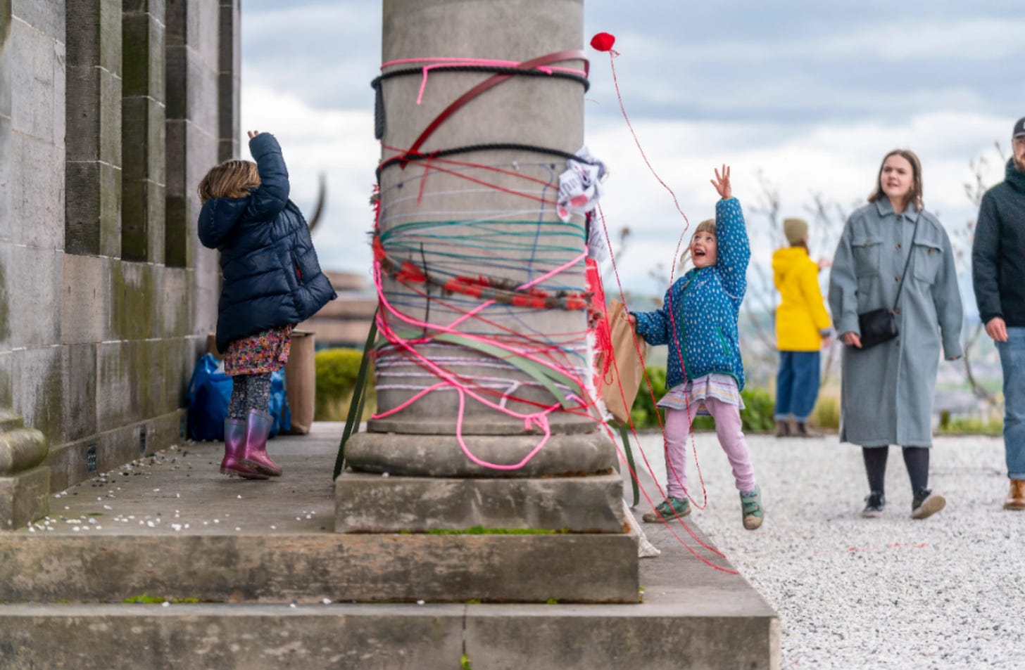little girls playing with yarn, wrapping it round a stone column on Calton Hill, Edinburgh