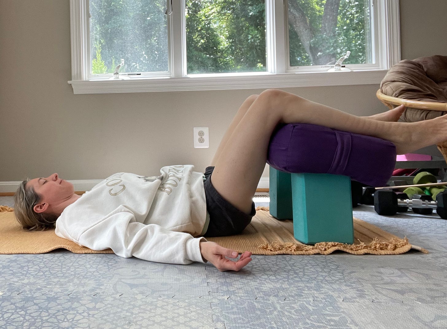 Woman lying on the ground resting her legs over a bolster that is propped up on two vertical-standing blocks