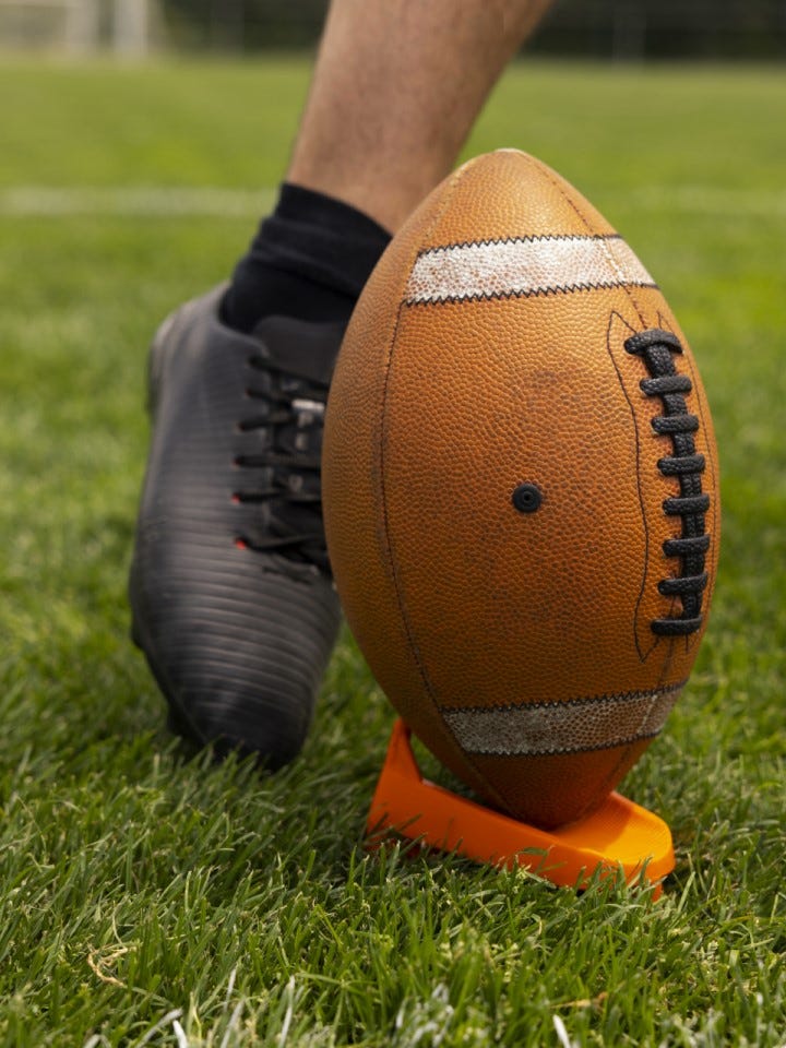 Closeup of a foot about to make contact with a football that's been placed on a tee.