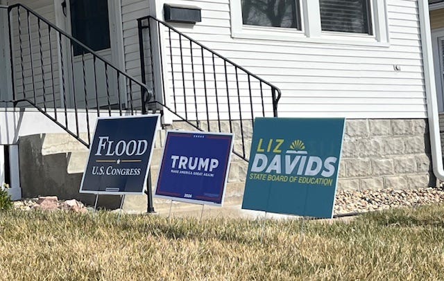 Three political signs in a front yard: Flood for US Congress, Trump 2024, and Liz Davids for State Board of Ed
