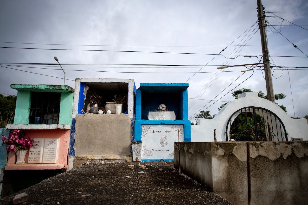 a cemetery in Pomuch, Yucatan, where people keep the mayan dia de muertos tradition and displaying remains of their passed away beloved ones. skulls are sitting on a colorfoul tombs