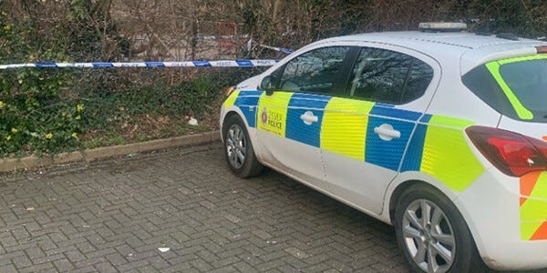 Police car parked near to the crime scene with tape marking the area