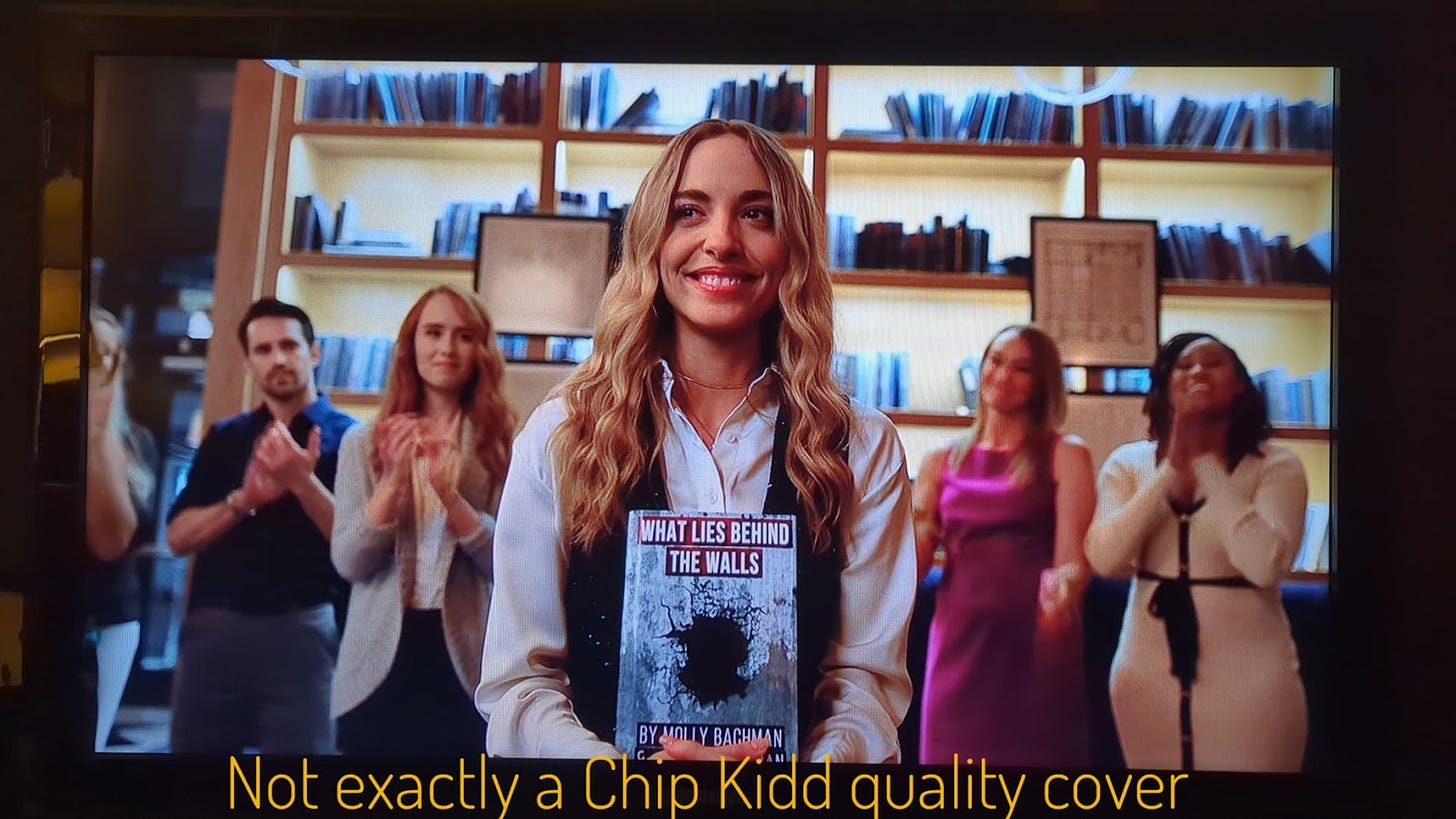 Molly holding her book while people clap around her, captioned "Not exactly a Chip Kidd quality cover" because it's pretty shoddy