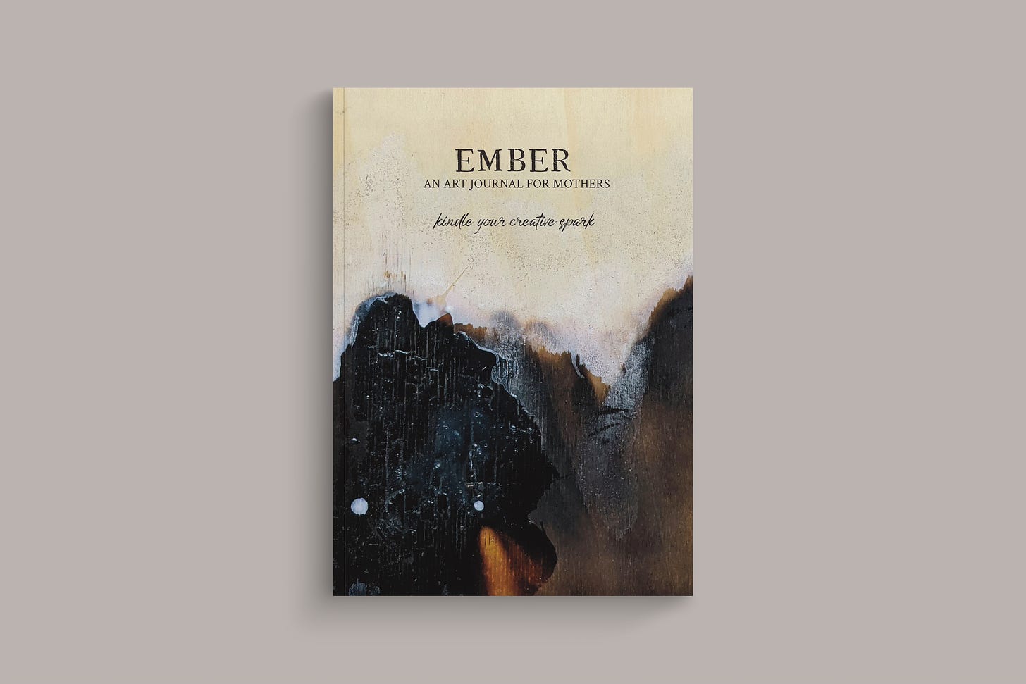 Mock up of Ember an art journal for mothers. Cover is charred wood. Script text below the title reads Kindle your creative spark.