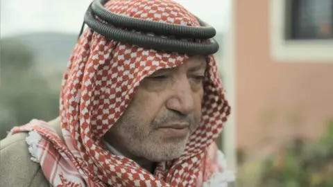 Matthew Cassel / BBC Nabil in a red and white checked headdress looking pensively at the floor 