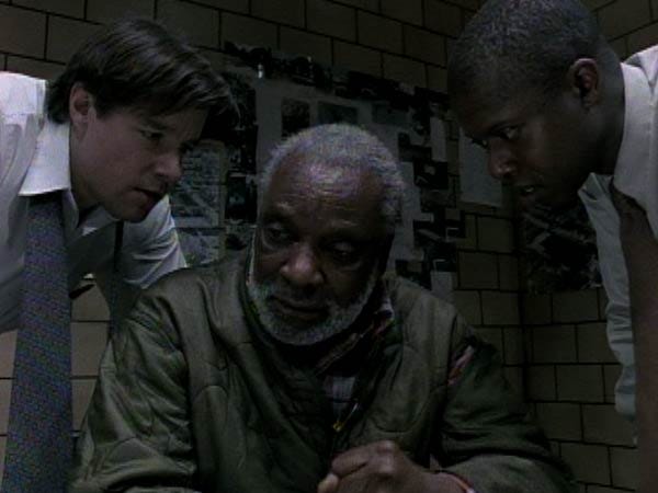 This still image shows Detective Tim Bayliss (played by Kyle Secor) and Detective Frank Pembleton (played by Andre Braugher) looming over Risley Tucker (played by Moses Gunn) in the Season 1 Homicide: Life on the Street episode "Three Men and Adena." Tucker sits at a table in the Baltimore Homicide Unit's primary interrogation room ("The Box"), looking down and to his right. Bayliss leans over Tucker's right shoulder, while Pembleton leans over Tucker's left shoulder. This still image shows Detective Tim Bayliss (played by Kyle Secor) and Detective Frank Pembleton (played by Andre Braugher) looming over Risley Tucker (played by Moses Gunn) in the Season 1 Homicide: Life on the Street episode "Three Men and Adena." Tucker sits at a table in the Baltimore Homicide Unit's primary interrogation room ("The Box"), looking down and to his right. Bayliss leans over Tucker's right shoulder, while Pembleton leans over Tucker's left shoulder.