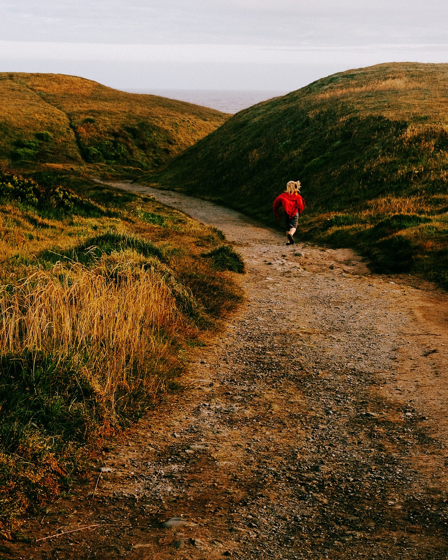 a 9-year-old runs down a canyon path with grassy hills on either side