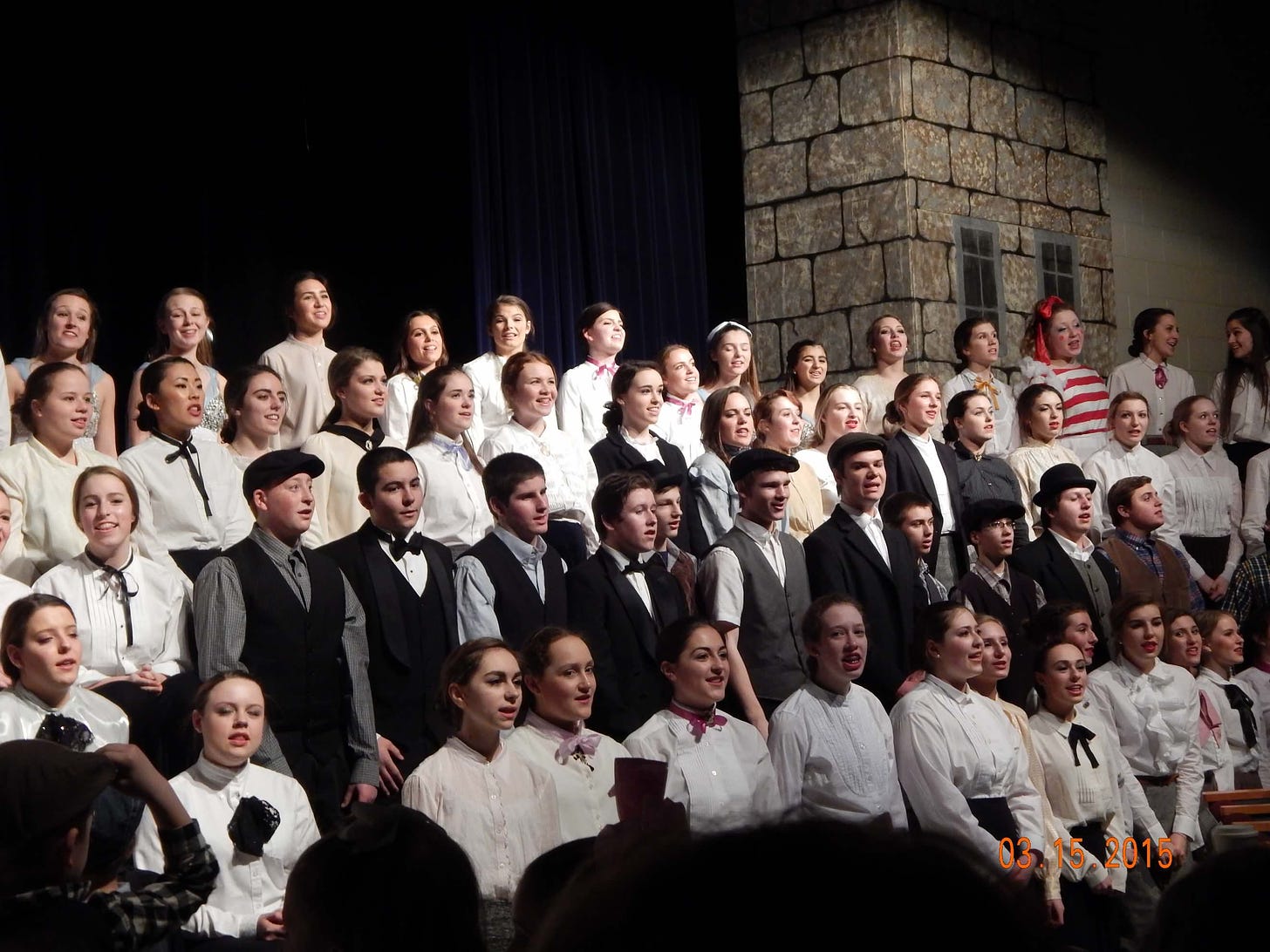 Dozens of high school students standing on a stage, dressed in costume to perform "Mary Poppins"