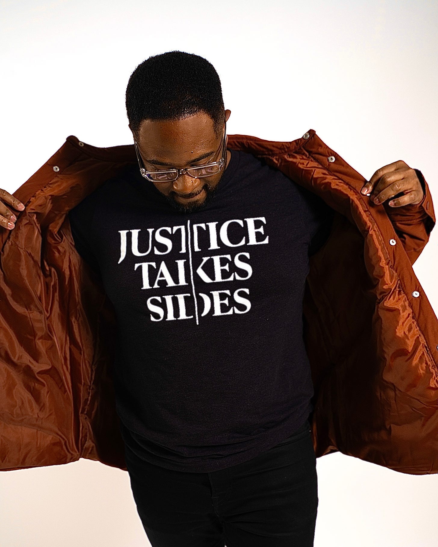 Photo of Jemar Tisby in front of white background wearing black "Justice Takes Sides" shirt