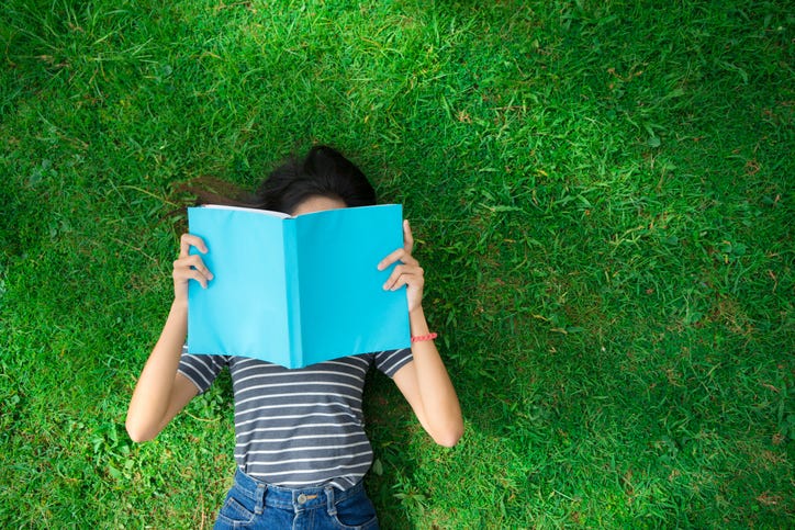 child lying on grass while reading