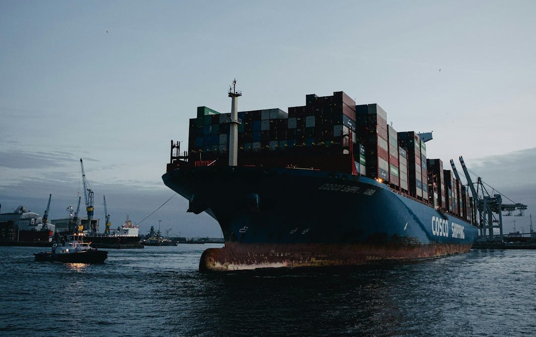 a large cargo ship in the ocean with a tug boat nearby a large cargo ship in the ocean with a tug boat nearby