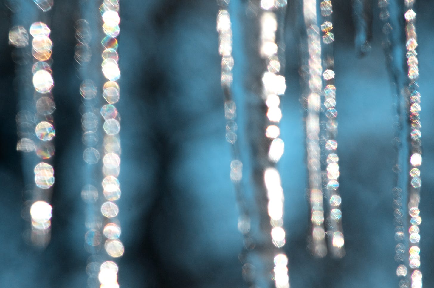 An abstract image uses a soft focus on an icicle forest, with teal shadowy background and vertical stripes of diamond-shimmer bokeh.