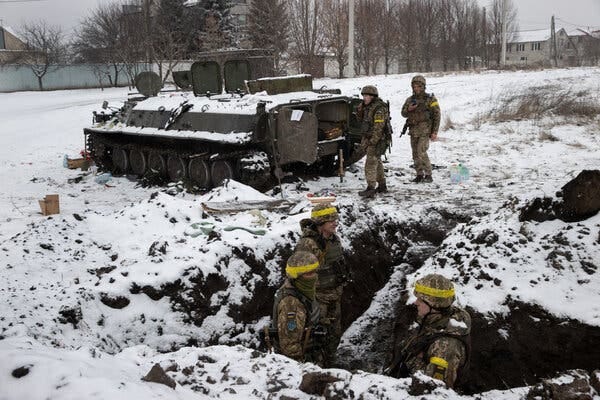 Ukrainian soldiers in uniform standing near a tank and in a trench in the snow.