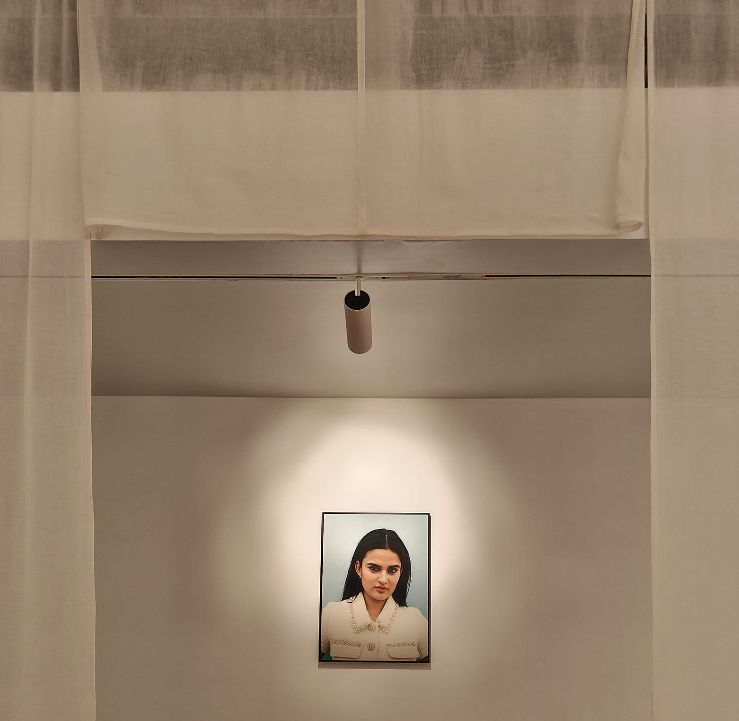 Prarthna Singh's portrait of a young woman on a white wall, spotlit and framed by white curtains.
