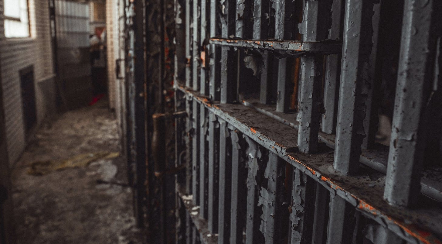 A rusting old prison door, paint peeling, looms in the image.
