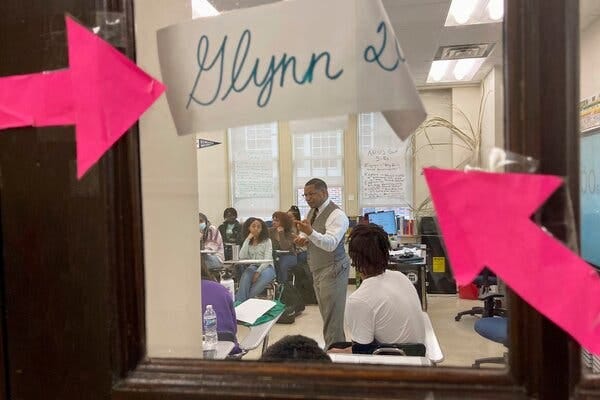 Through a window, a teacher leads a class of students. 