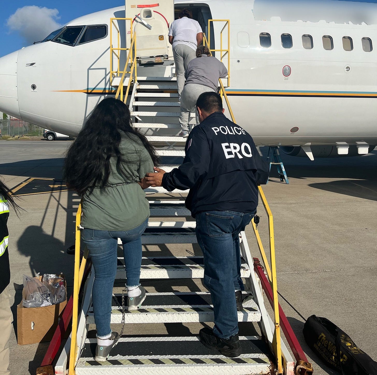 An ICE “Enforcement & Removal Operations” (ERO) Officer escorts a woman who was in the US illegally onto an airplane bound for Honduras in Harlingen, Texas (July 2024) An ICE “Enforcement & Removal Operations” (ERO) Officer escorts a woman who was in the US illegally onto an airplane bound for Honduras in Harlingen, Texas (July 2024)