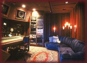 A photo of a recording studio with a rug and blue couch behind the large soundboard