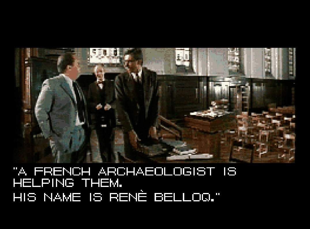 A screenshot of a cutscene from Greatest Adventures, which is a static image from the film Raiders of the Lost Ark placed into the game. Indiana Jones, dressed in his professor's suit and wearing glasses, is speaking with Dr. Marcus Brody at the university where he works. The text reads, "A French archaeologist is helping them. His name is René Belloq."